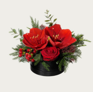 Söt julgrupp i rund liten hattask. Låg dekoration med amaryllis, rosor, röda bär och grönt. Skicka julblommorna med ett bud från Interflora!
