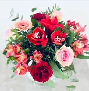 Julbukett i rött, rosa och vitt, med blommor som amaryllis, rosor, germini, hyperikum, alstromeria, nejlika och så lite grönt på det. Blommorna finns hos Made4y.se.